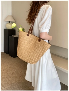 Close-up of woven straw tote bag featuring brown leather handles and natural texture