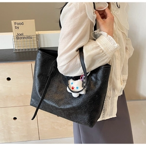 Detail of black tote bag with embossed patterns and a white cloud plush charm