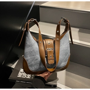 Détail du sac en jean bleu et cuir marron avec œillets métalliques et boucle