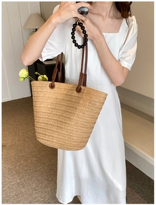 Close-up of a large woven straw tote bag with brown leather straps and floral accents