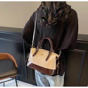 Detail of two-tone beige and brown Boston bag featuring golden logo and leather handles