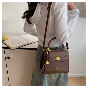 Detailed close-up of dark brown leather crossbody bag with golden dog metal buckle detail