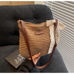 Detailed close-up of woven straw handbag featuring a lace bow and brown leather strap