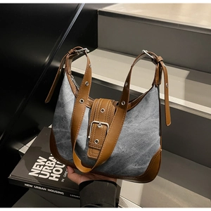 Détail du sac à bandoulière en denim délavé avec finitions en cuir marron et œillets