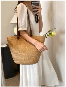 Detail of woven straw tote bag featuring brown leather strap and floral interior decoration
