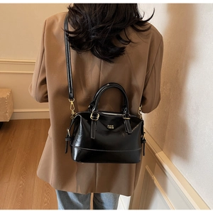 Detail of black glossy Boston bag with white stitching and gold hardware on model