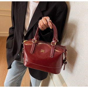 Detail of burgundy Boston handbag with gold logo and cylindrical handles on casual model