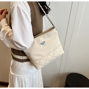 Detail of cream woven bucket bag featuring diamond quilting and metal triangle logo