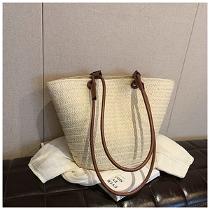 Detail of French straw tote bag with brown faux leather handles and woven texture on a bench