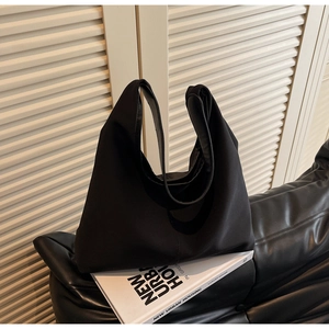 Detail of a black minimalist canvas tote bag resting on a leather sofa in soft lighting