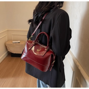 Fashionable dark burgundy Boston bag with golden logo worn by model in black suit