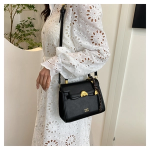 Detail of black leather handbag with gold lion head buckle and woven pendant detail