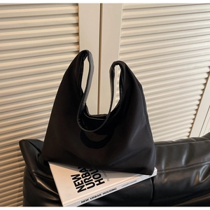 Detail view of large black canvas tote bag on a leather cushion with soft shadows