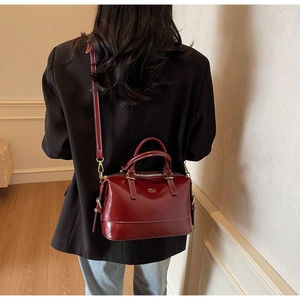 Detail of burgundy Boston bag with contrast white stitching and gold-tone hardware