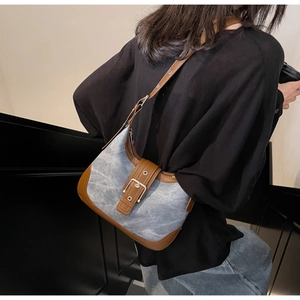 Détail du sac à bandoulière en jean bleu avec finitions en cuir brun et boucle métal