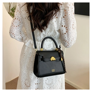 Detail of black leather handbag featuring a gold poodle buckle on white lace dress