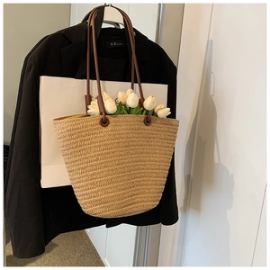 Detail of woven straw tote bag with brown handles hanging on a black suit blazer