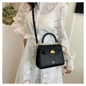 Detail of black leather handbag with golden lion head buckle and crossbody strap style