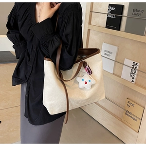 Detail of cream tote bag with embossed texture, brown straps, and star plush charm detail