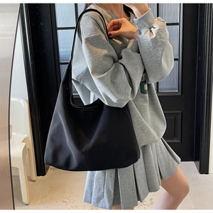 Side view of a minimalist black canvas shoulder bag worn by a model in a modern interior