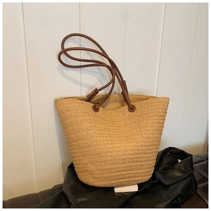 Close-up of woven straw tote bag featuring thick brown rope straps and leather accents