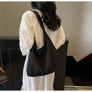 Side view of large black minimalist tote bag worn by model over a white textured dress