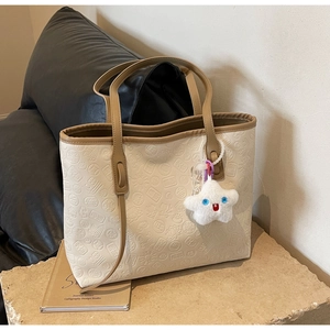 Detail of off-white tote bag with embossed lucky symbols and a star plush charm