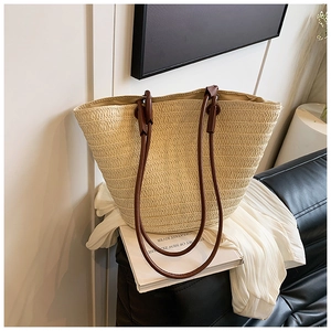 Close-up of woven straw tote bag featuring brown leather handles on a minimal sofa