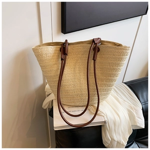 Detail of handwoven straw tote bag with brown leather straps on a modern sofa
