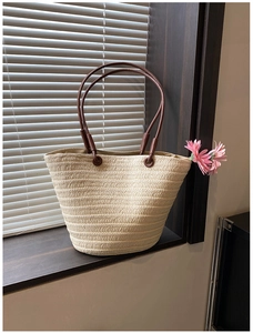 Close-up of beige woven straw tote bag with brown leather handles and pink flower detail