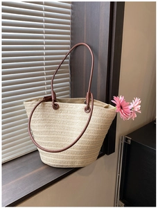 Detail of hand-woven straw tote bag featuring brown PU handles and natural texture