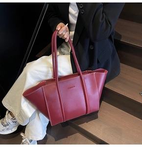 Detailed view of dark red leather tote bag with white contrast stitching and fashion text