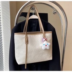 Detail of cream tote bag with embossed lucky symbols and brown strap on blazer