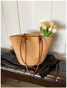 Close-up of woven straw tote bag with brown handles and white tulip decor on leather seat