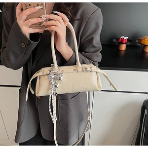 Chic beige Boston bag detail with metallic eyelets and bow tassel charm on a model