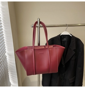 Close-up of burgundy tote bag with white contrast stitching and embossed logo detail