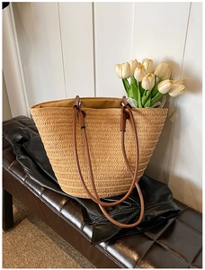 Detail view of woven straw tote bag with brown leather handles and dark fabric lining