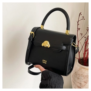 Detail of black leather handbag with golden poodle hardware and refined matte texture