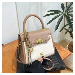 Detail view of khaki and cream crossbody bag with a golden dog-shaped magnetic clasp