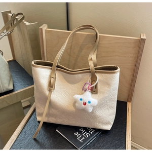 Detail of embossed cream tote bag featuring a star plush charm and slender brown handles