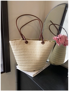 Detail of hand-woven straw tote bag featuring brown leather handles and textured ivory finish