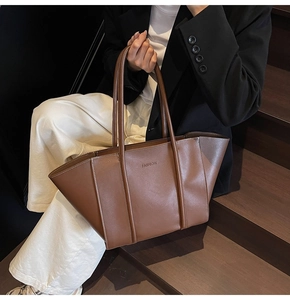 Detail of a large brown leather tote bag with FASHION logo and wide winged design