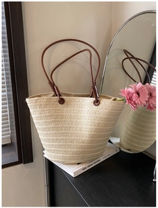 Detail of hand-woven straw tote bag with brown leather straps and metal rivets