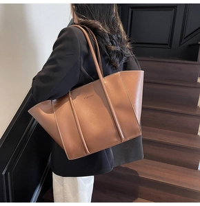 Model wearing a large tan faux leather tote bag with FASHION lettering on wooden stairs