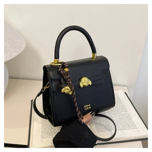 Close-up of black handbag with golden dog head ornaments and logo on a book base