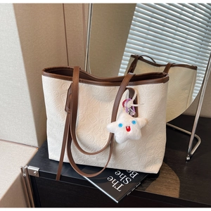 Detail of white embossed tote bag with brown straps and a plush star pendant