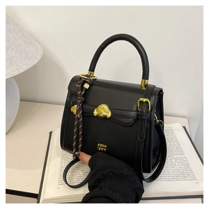 Detail of black leather handbag featuring golden animal buckle and decorative woven strap