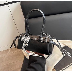 Detail of a mini black leather Boston bag with metal buckle and silver bow pendant