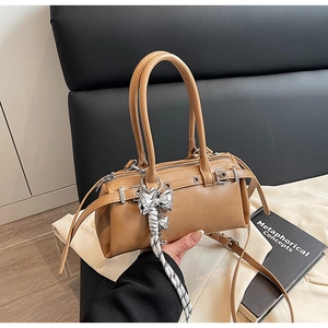 Caramel Boston bag with rivet details and knitted bow charm on black leather chair