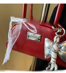 Détail d'un sac rouge avec ferrures argentées et breloque en dentelle blanche